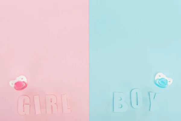 Top view of pacifiers, boy, girl lettering on pink and blue background with copy space — Stock Photo