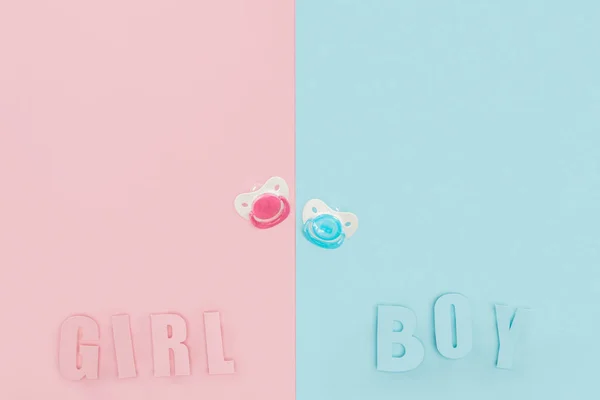 Top view of pacifiers, boy, girl lettering on pink and blue background with copy space — Stock Photo