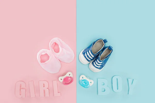 Top view of pacifiers, booties, sneakers and boy, girl lettering on pink and blue background — Stock Photo