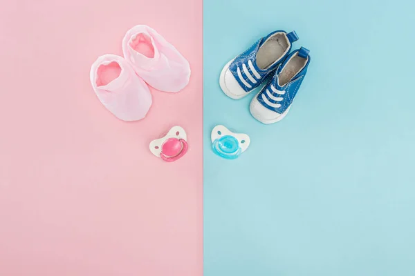 Top view of pacifiers, booties, sneakers on pink and blue background with copy space — Stock Photo