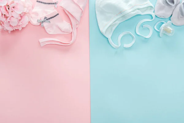 Top view of pacifier, bonnets, booties, socks, bouquet on pink and blue background — Stock Photo