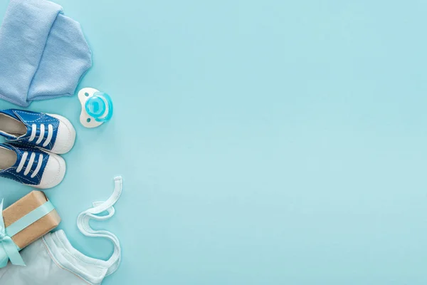 Top view of pacifier, gift, sneakers, bonnet, hat on blue background with copy space — Stock Photo