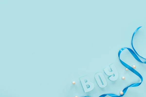 Top view of ribbon, pearls and boy lettering on blue background with copy space — Stock Photo