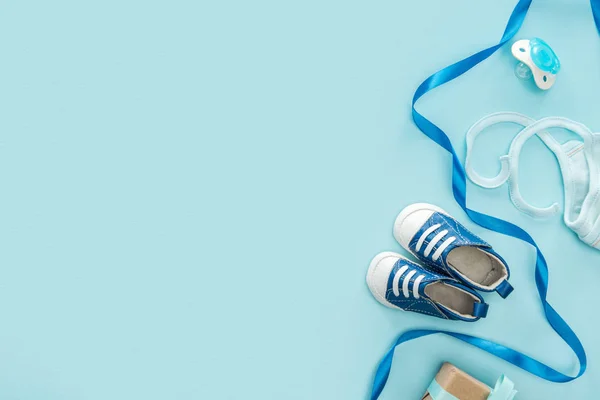 Vista superior de chupeta, presente, sapatilhas, capota, fita no fundo azul com espaço de cópia — Fotografia de Stock