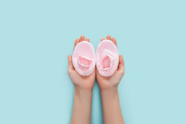 Partial view of adult woman holding pink booties on blue background with copy space — Stock Photo