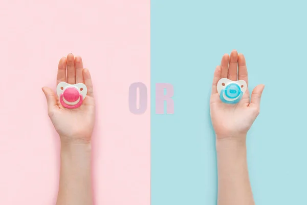 Partial view of women holding pacifiers with or lettering on blue and pink background — Stock Photo