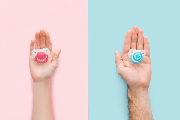 Partial view of woman and man holding pacifiers on blue and pink background — Stock Photo