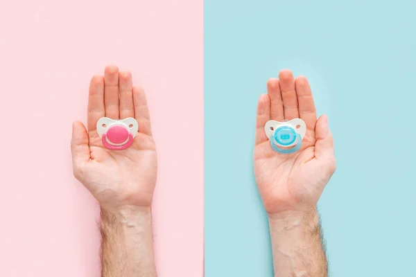 Cropped view of men holding pacifiers on blue and pink background with copy space — Stock Photo