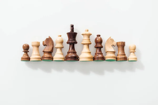 Вид сверху на ряд из коричневых и бежевых деревянных шахматных фигур на белом фоне — стоковое фото