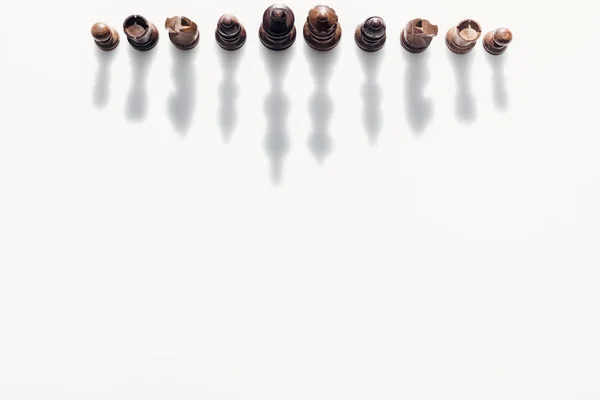 Vista superior de figuras de ajedrez marrones con sombras sobre fondo blanco - foto de stock
