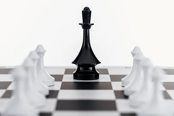 Foco seletivo de tabuleiro de xadrez com figura rainha preta entre peões brancos isolados em branco — Fotografia de Stock