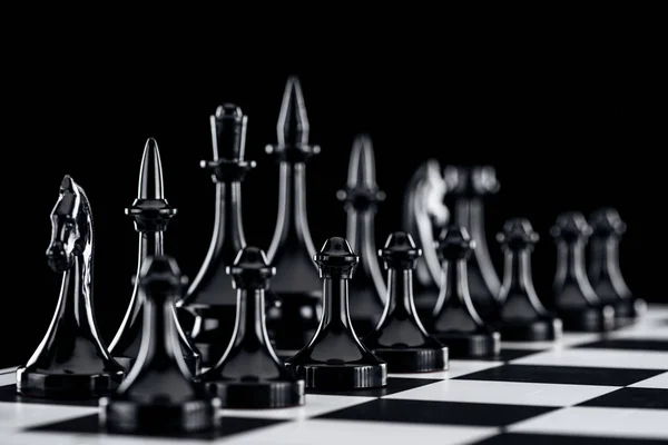 Enfoque selectivo de tablero de ajedrez con figuras de ajedrez negro aisladas en negro - foto de stock