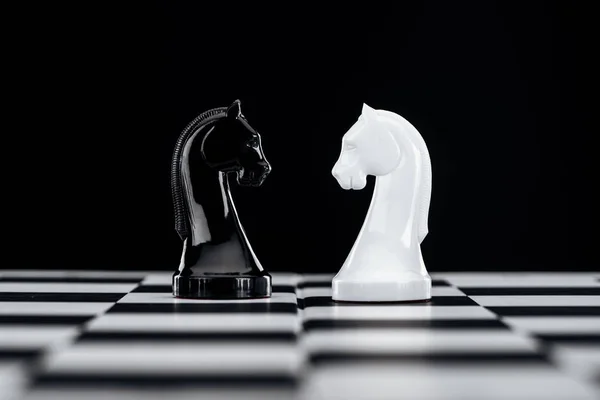 Selective focus of chessboard with white and black knights isolated on black — Stock Photo