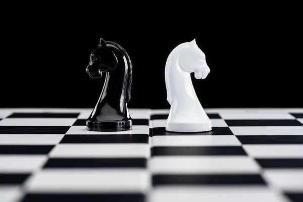 Selective focus of chessboard and white and black knights isolated on black — Stock Photo
