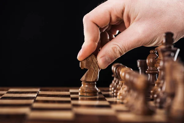 Cropped view of man doing move with knight on wooden chessboard isolated on black — Stock Photo