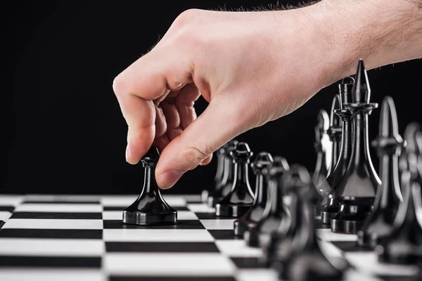 Cropped view of man doing move with pawn on chessboard isolated on black — Stock Photo