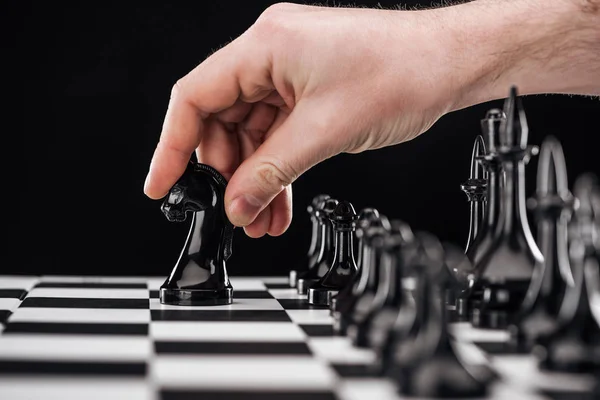 Cropped view of man doing move with knight on chessboard isolated on black — Stock Photo