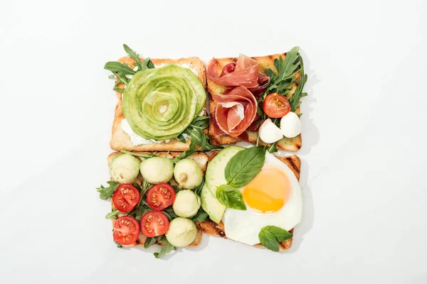 Top view of toasts with cut vegetables and prosciutto on white surface — Stock Photo
