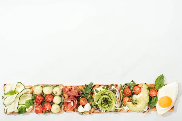 Top view of toasts with cut vegetables, fried egg and prosciutto on white surface — Stock Photo