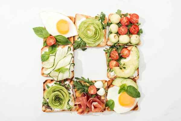 Vue de dessus des toasts aux légumes coupés, œufs frits et prosciutto à la surface blanche — Photo de stock