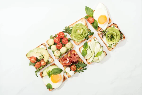 Vue de dessus des toasts aux légumes coupés, œufs frits et prosciutto à la surface blanche — Photo de stock