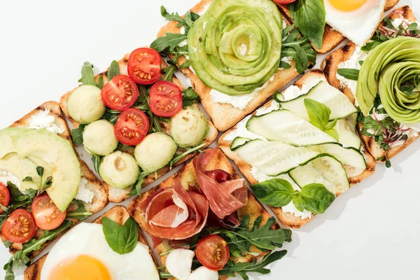 Top view of toasts with cut vegetables, fried eggs and prosciutto on white — Stock Photo