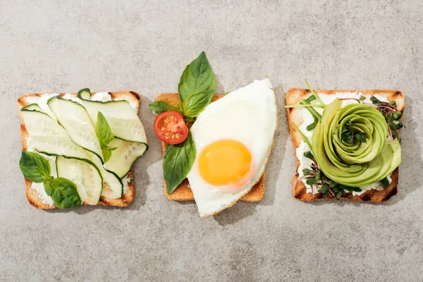 Top view of toasts with vegetables, basil and fried egg on textured surface — Stock Photo