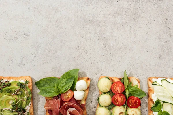 Vue de dessus des toasts aux légumes coupés et au prosciutto sur surface texturée — Photo de stock