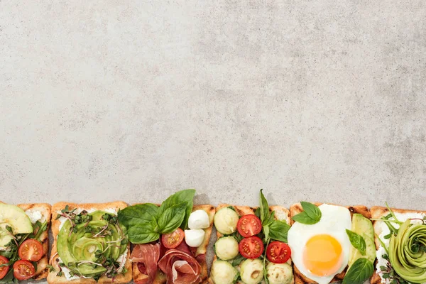 Vista superior de torradas com legumes cortados e prosciutto na superfície texturizada — Fotografia de Stock