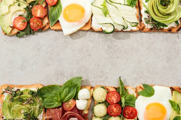 Вид сверху на тосты с овощами, жареными яйцами и prosciutto на текстурированной поверхности — стоковое фото