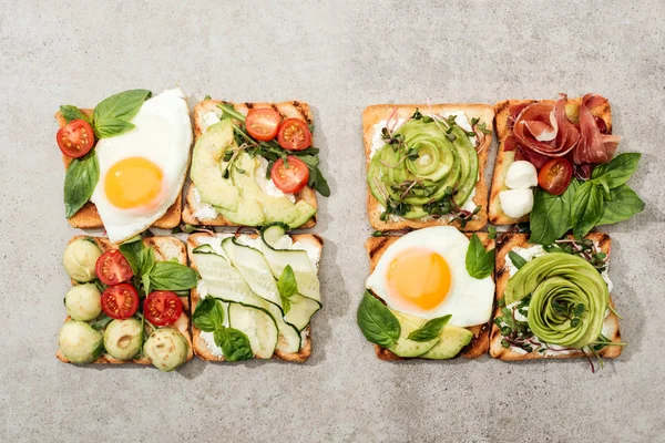 Top view of toasts with vegetables, fried eggs and prosciutto on textured surface — Stock Photo