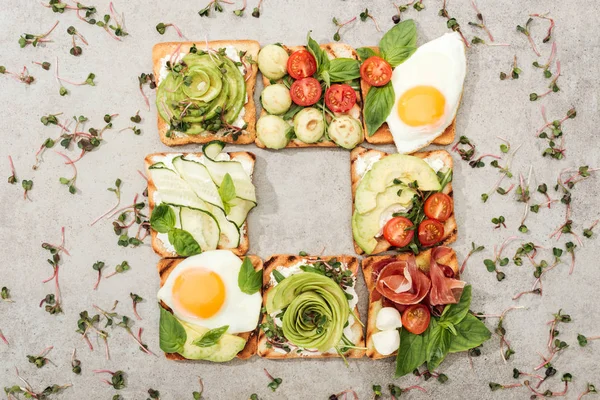 Top view of toasts with vegetables, fried eggs and prosciutto on textured surface — Stock Photo