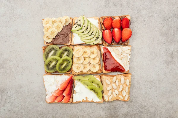 Vue de dessus des toasts aux fruits coupés, baies et arachides sur surface texturée — Photo de stock