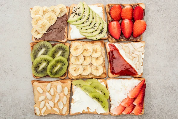 Vista superior de torradas com frutas cortadas, bagas e amendoins na superfície texturizada — Fotografia de Stock