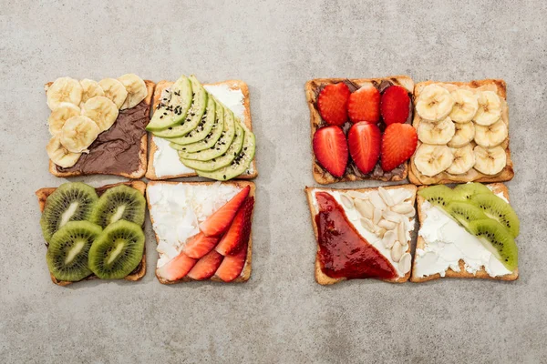Vista superior de torradas com frutas cortadas, bagas e amendoins na superfície texturizada — Fotografia de Stock
