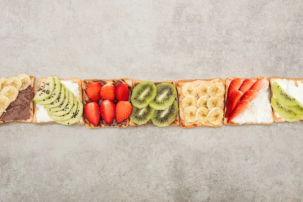 Vista dall'alto dei toast con frutta tagliata, bacche e arachidi sulla superficie testurizzata — Foto stock
