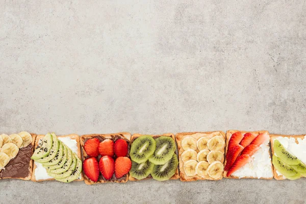 Top view of toasts with cut fruits, berries and peanuts on textured surface — Stock Photo