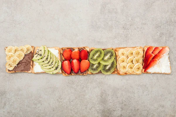 Vista dall'alto di pani tostati con frutta tagliata e bacche su superficie strutturata — Foto stock