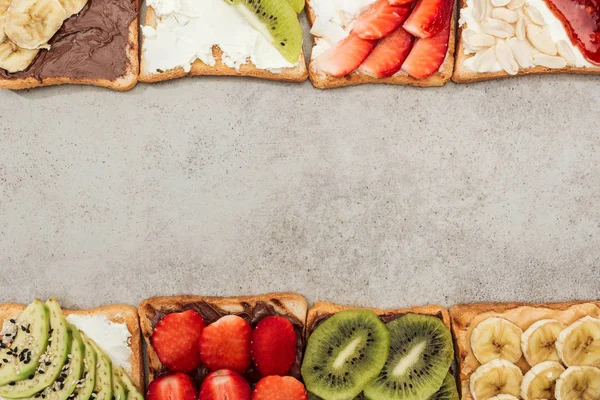 Vista dall'alto di pani tostati con frutta tagliata e bacche su superficie strutturata — Foto stock