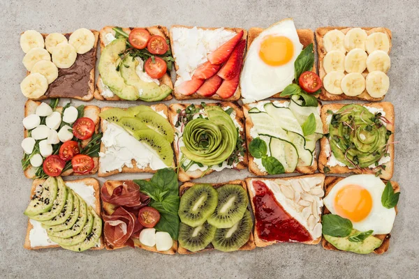 Вид сверху на тосты с жареными яйцами, нарезанными овощами и фруктами на текстурированной поверхности — стоковое фото