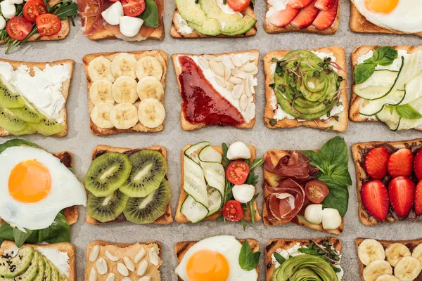 Top view of toasts with fried eggs, cut vegetables and fruits on textured surface — Stock Photo