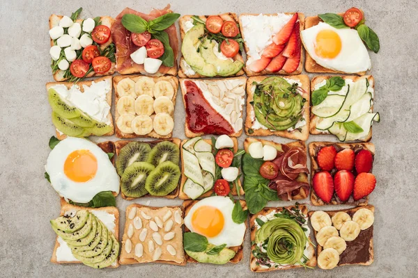 Top view of toasts with fried eggs, cut vegetables and fruits on textured surface — Stock Photo