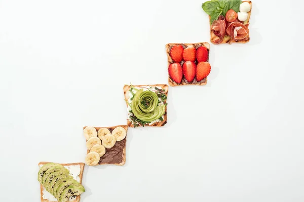 Top view of toasts with cut fruits, strawberry and prosciutto on white surface — Stock Photo