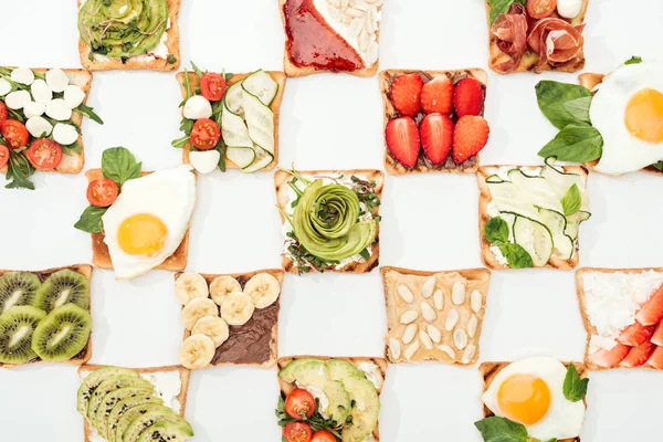 Вид сверху на тосты с нарезанными фруктами, овощами и арахисом на белой поверхности — стоковое фото