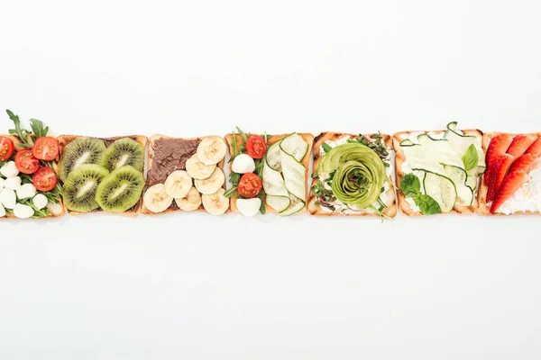 Top view of toasts with cut fruits, vegetables and peanuts on white — Stock Photo