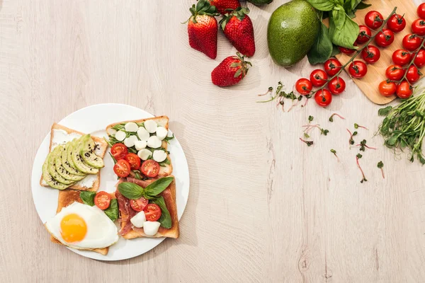 Vue du dessus de délicieux toasts avec légumes sur assiette et ingrédients frais sur table en bois — Photo de stock