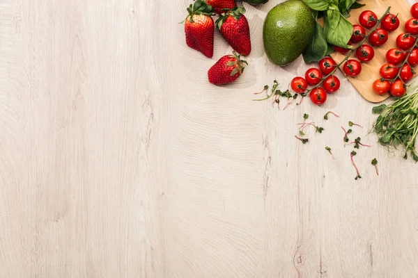 Вид зверху на полуницю, вишневі помідори, авокадо і базилік на дерев'яному столі з місцем для тексту — стокове фото