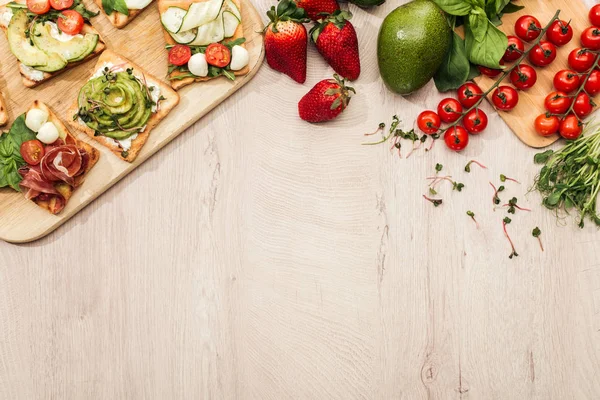 Top view of toasts with vegetables and prosciutto on wooden table with ingredients — Stock Photo