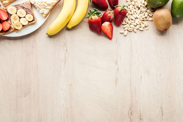 Top view of bananas, strawberries, peanuts and toasts on wooden table with copy space — Stock Photo