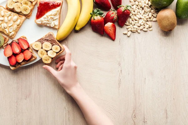 Верхний вид женщины с фруктовыми тостами за деревянным столом со свежими ингредиентами — стоковое фото